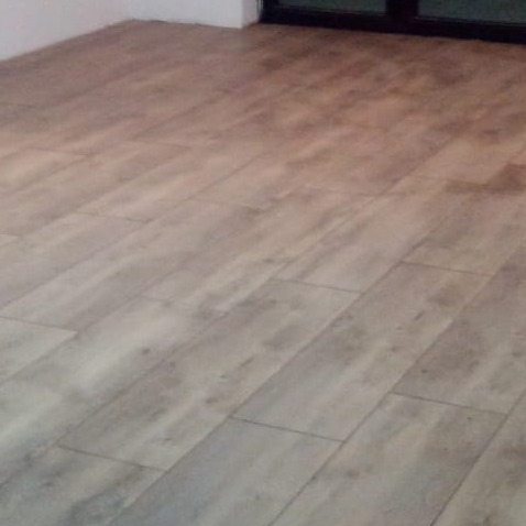 Ułożona pod kątem podłoga z paneli imitujących drewno w odcieniach szarości i beżu, widoczna część ściany i przesuwne drzwi balkonowe.