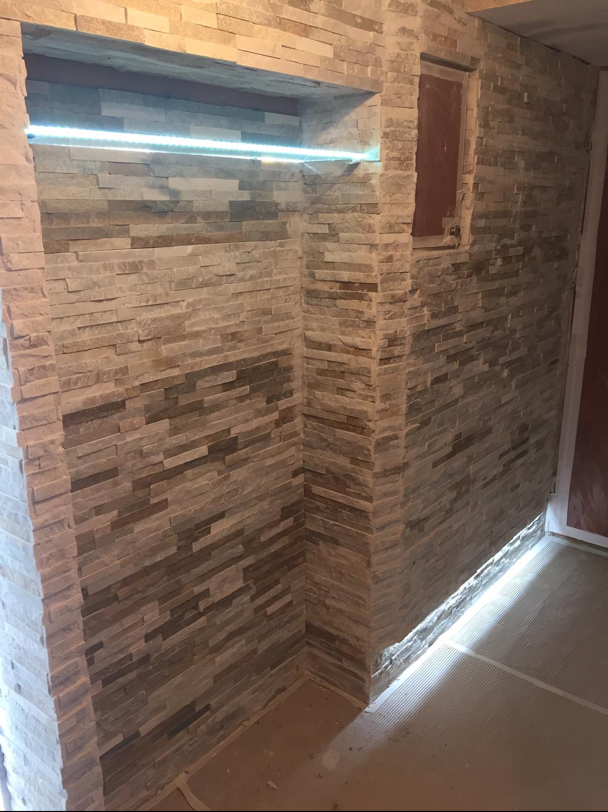 Ściana wyłożona dekoracyjnym kamieniem elewacyjnym w odcieniach beżu i brązu, z podświetloną wnęką LED i ukrytym otworem rewizyjnym, ukazująca efekt po remoncie.