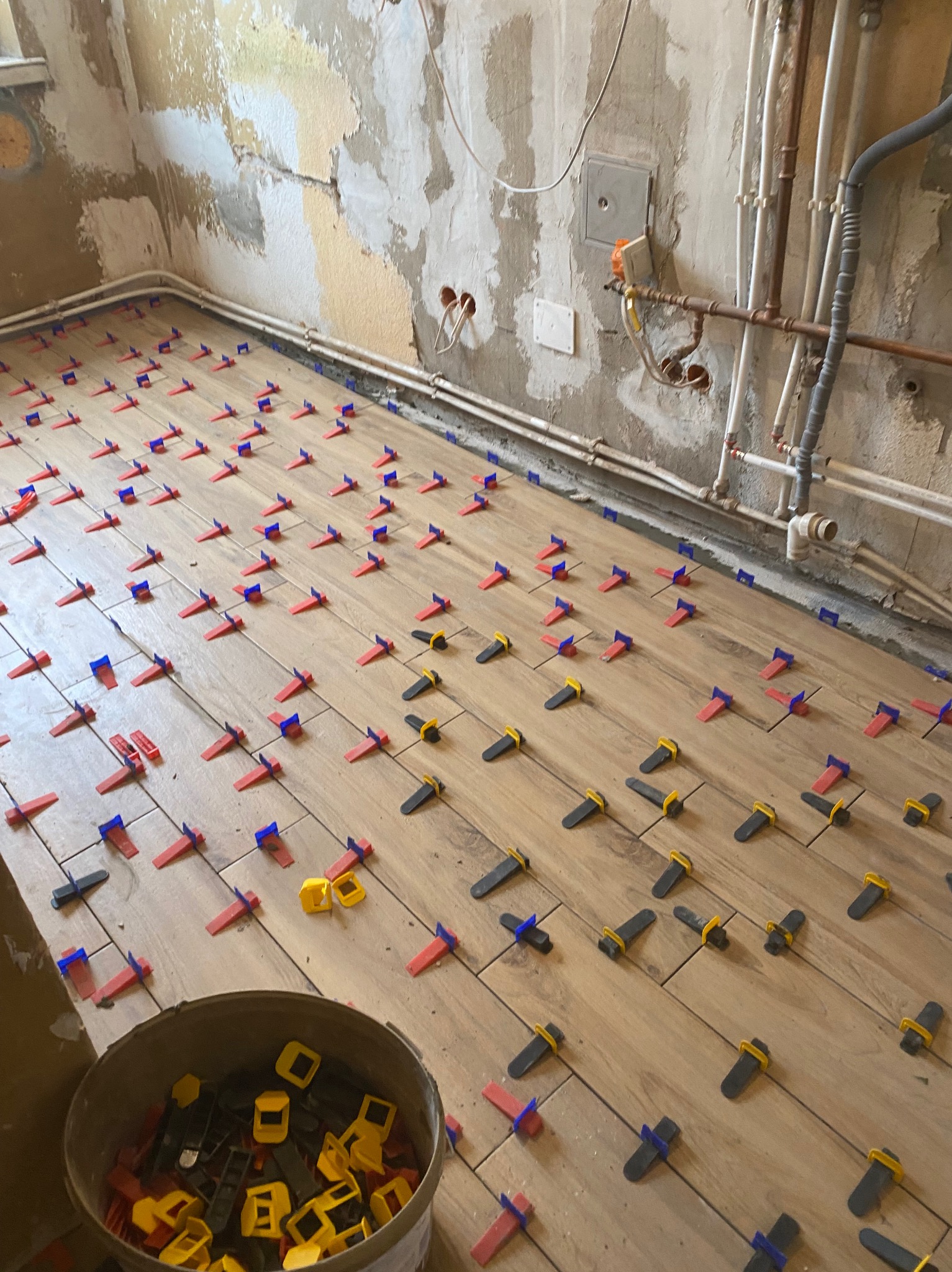 Układanie drewnopodobnych płytek z użyciem klipsów poziomujących na podłodze w trakcie remontu. Na ścianie widoczne instalacje i ślady po poprzednich warstwach wykończenia.