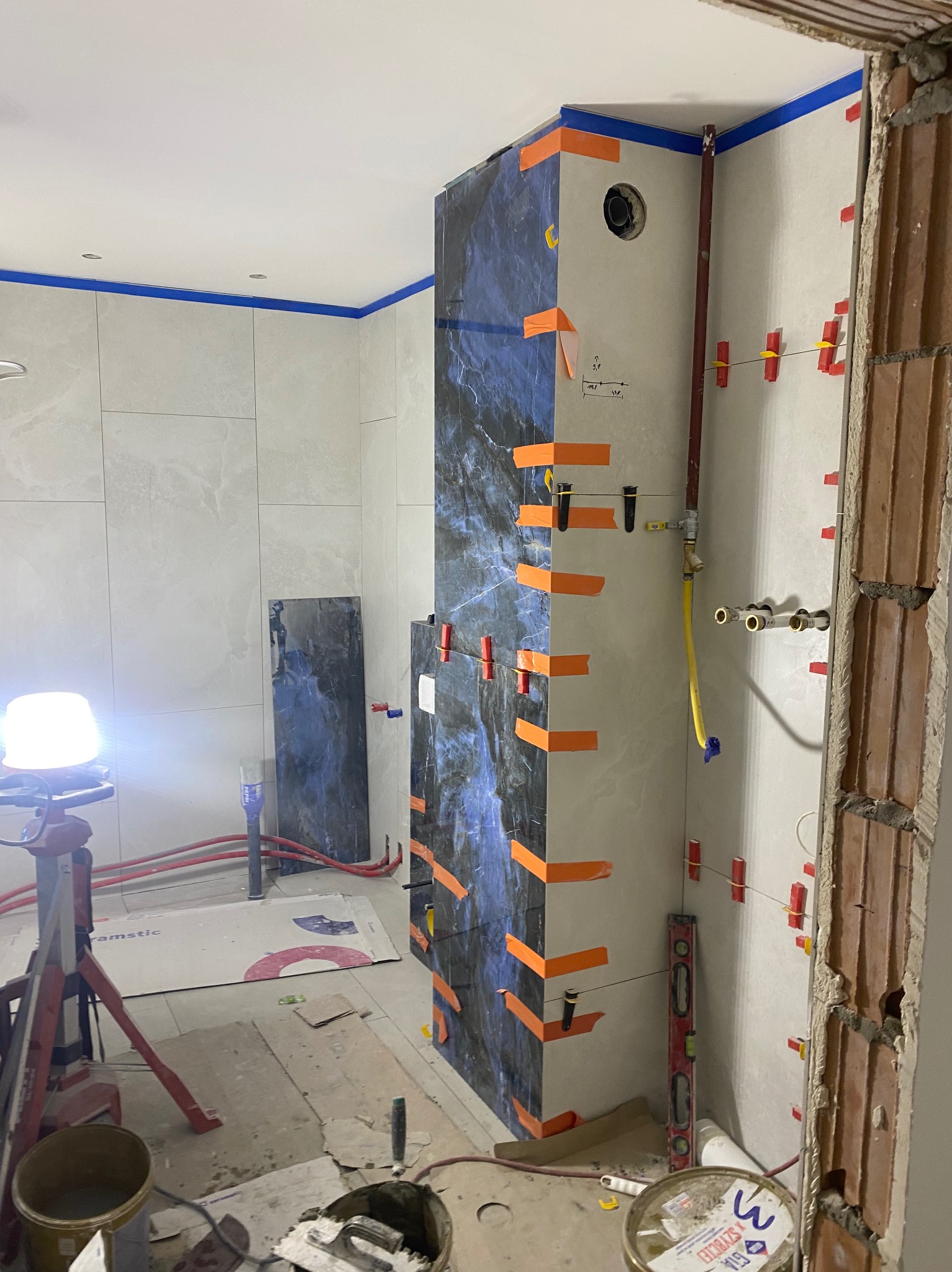 Łazienka w trakcie prac: układanie płytek imitujących marmur na ścianie, widoczne poziomice, szpachelki i inne narzędzia glazurnicze.