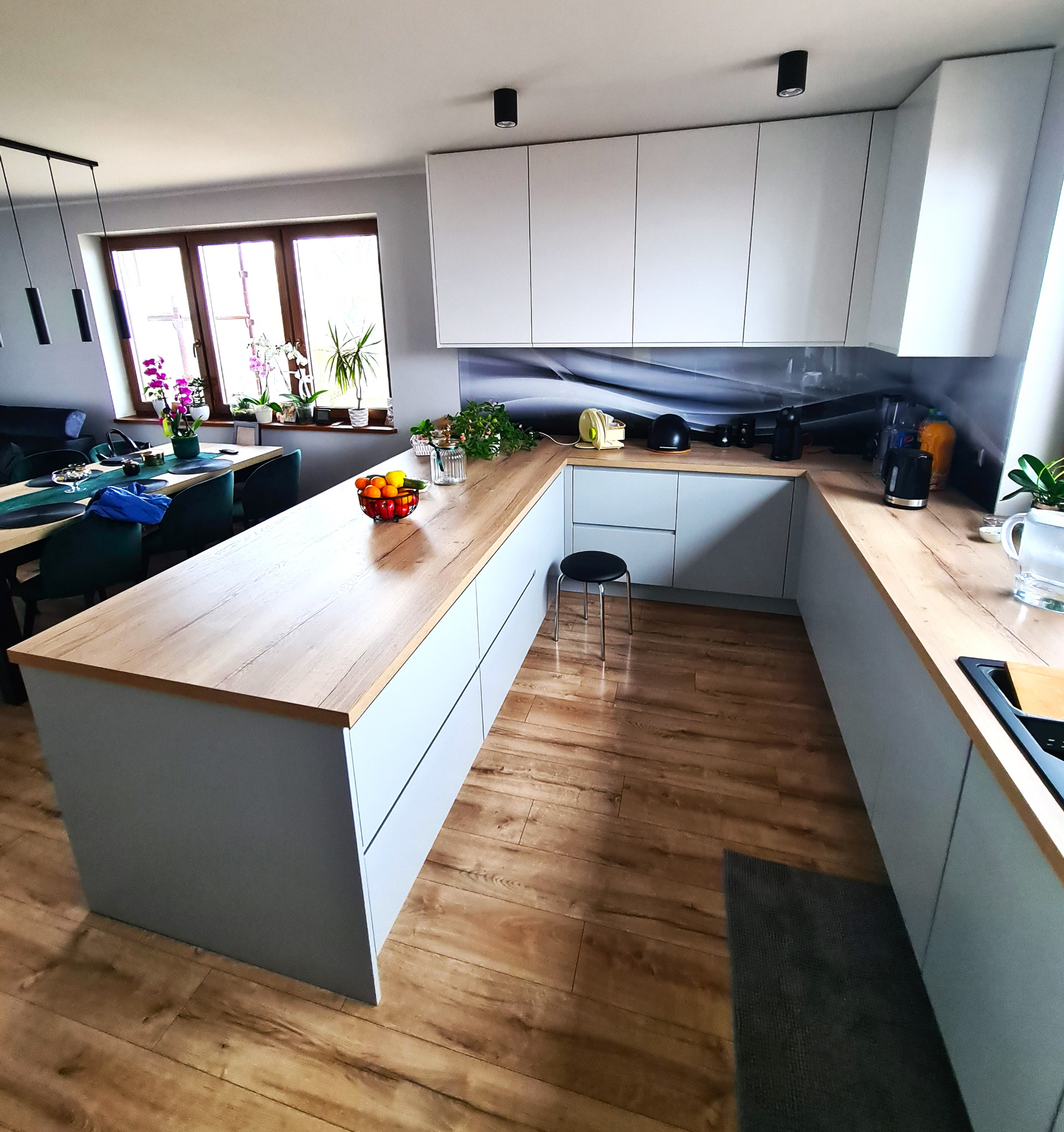 Jasna kuchnia z drewnianym blatem, wyspą i czarnymi lampami sufitowymi, widok z perspektywy podłogi.