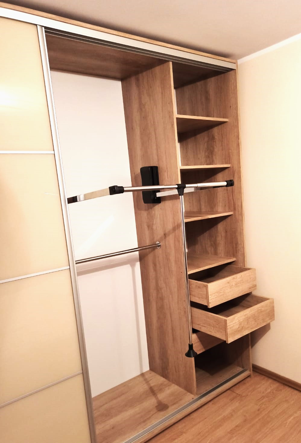 Wnętrze szafy wnękowej z przesuwnymi drzwiami, wykonanej z drewna w odcieniach beżu i brązu, z półkami, szufladami i drążkami na ubrania.