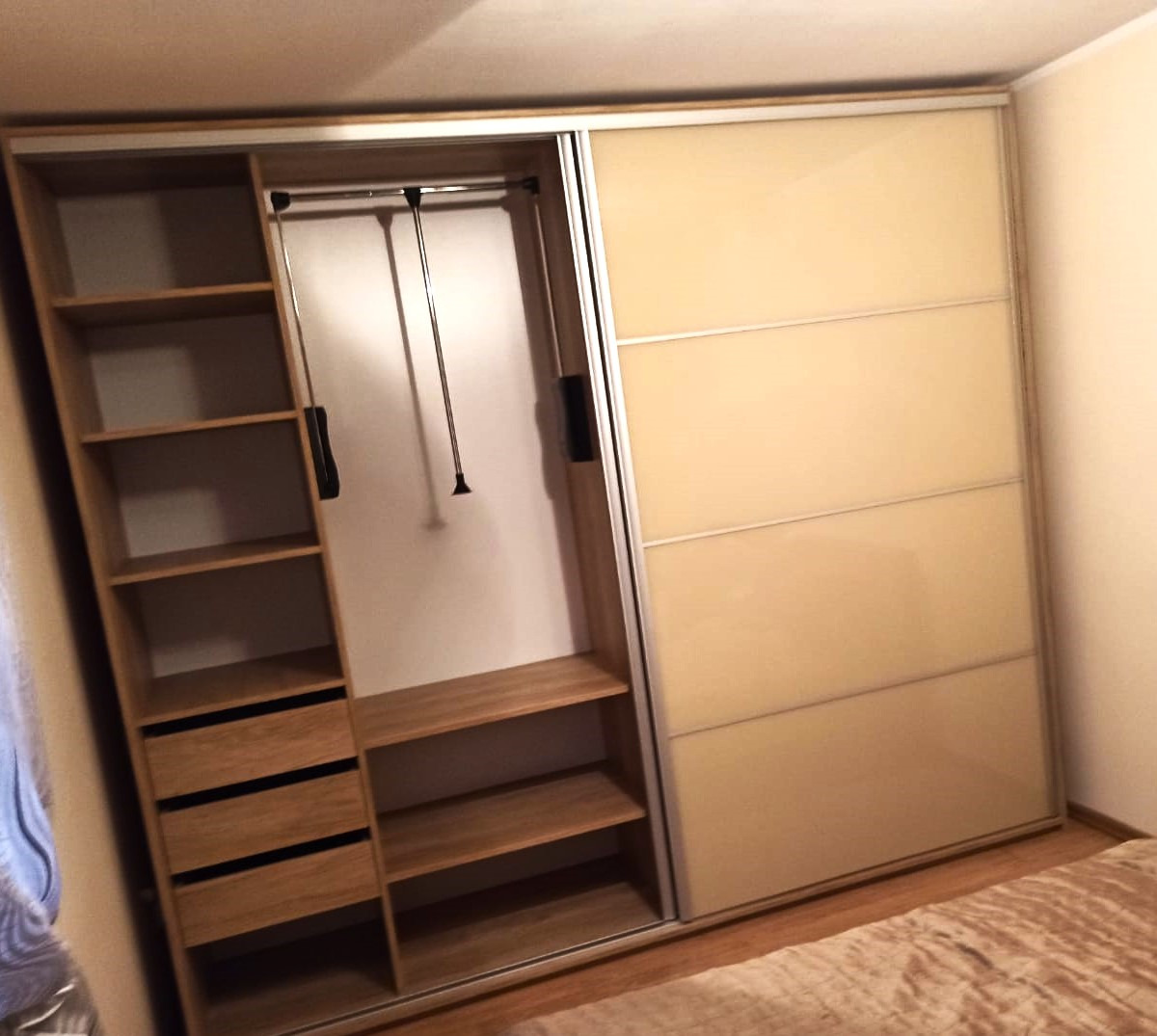 Beżowa szafa przesuwna z jasnego drewna z otwartą częścią ukazującą półki, szuflady i drążek na ubrania.