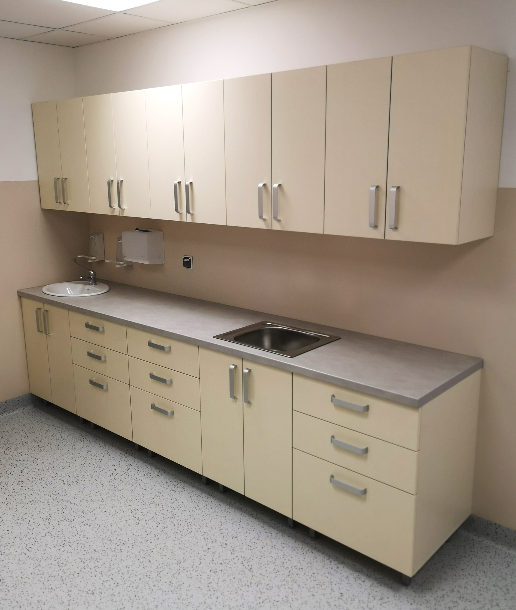 Beżowe szafki wiszące i stojące z szarym blatem i dwiema umywalkami w pomieszczeniu o neutralnym wystroju.