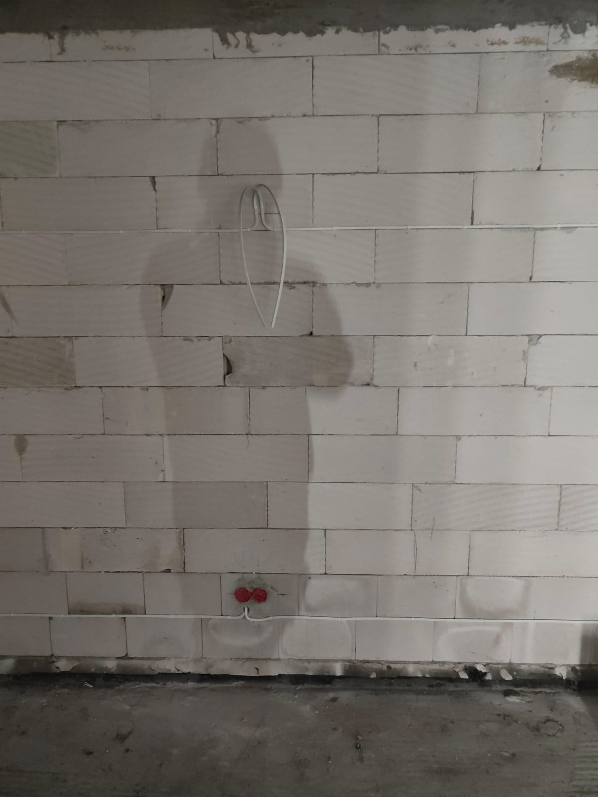 Surowa ściana z betonu komórkowego z poprowadzonym kablem elektrycznym i puszkami zabezpieczonymi czerwonymi zaślepkami. Kabel przymocowany do ściany za pomocą białych uchwytów.