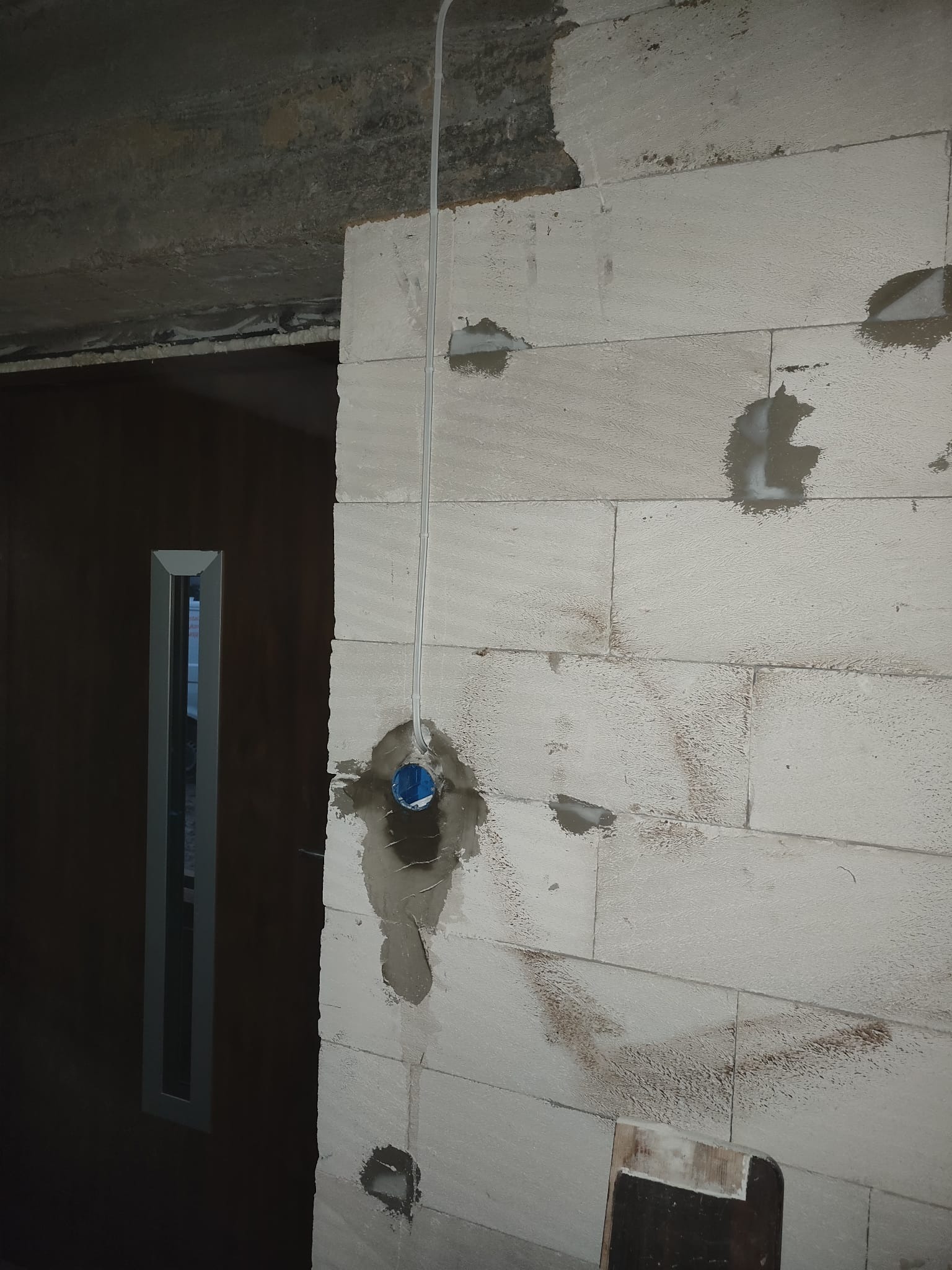 Wewnętrzna ściana z betonu komórkowego w trakcie prac instalacyjnych: puszka elektryczna zamontowana w ścianie, przewód elektryczny poprowadzony wzdłuż ściany, ślady zaprawy wokół puszki i...