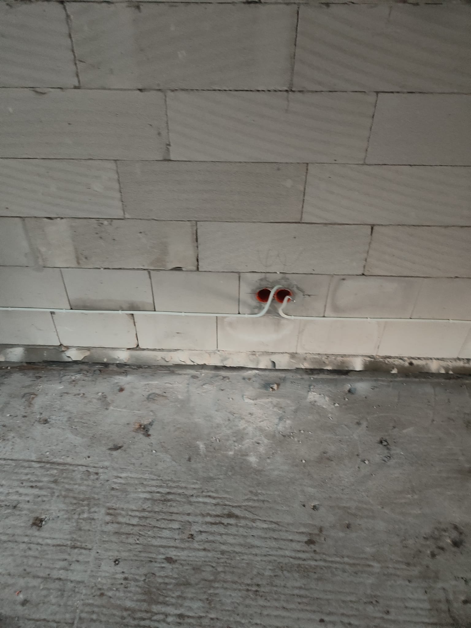 Wystające przewody elektryczne ze ściany z betonu komórkowego, widoczne pomarańczowe puszki instalacyjne.