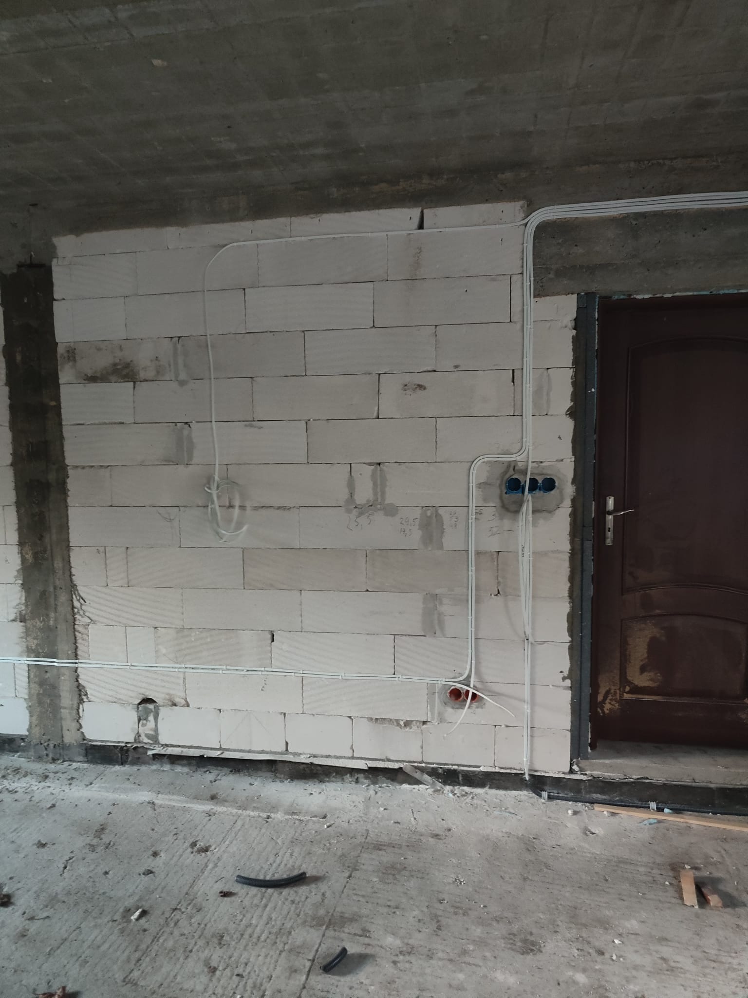 Surowy stan: instalacja elektryczna w ścianie z betonu komórkowego, przewody prowadzone natynkowo, widoczne puszki instalacyjne i fragment drzwi.