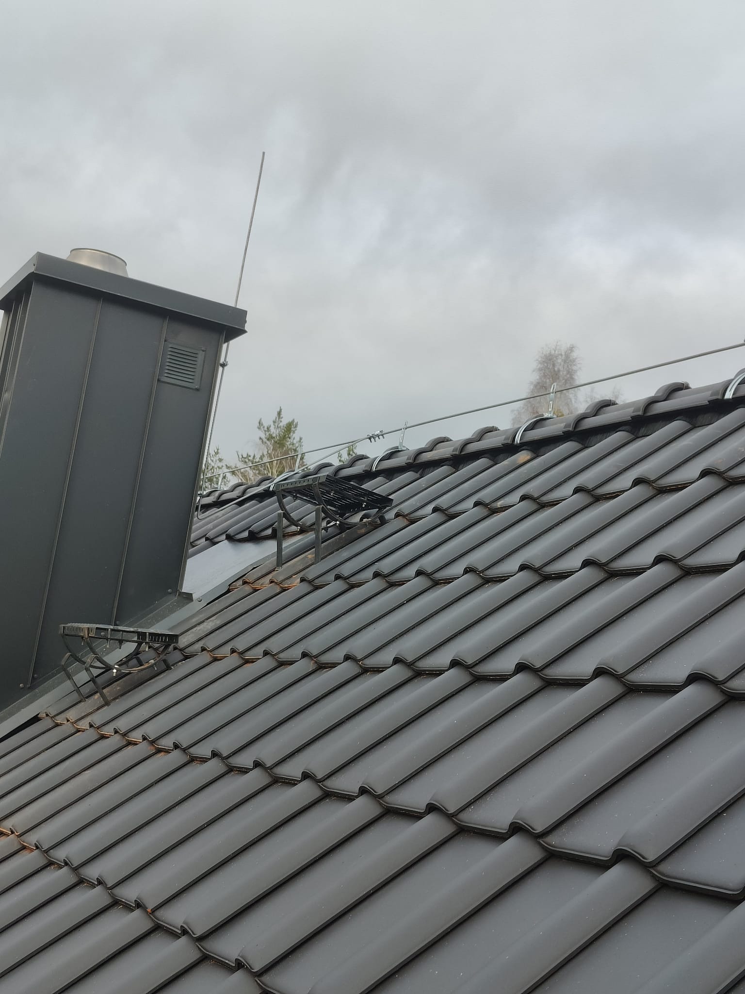 Szary dach z dachówki ceramicznej z zamontowaną instalacją odgromową, widoczny komin i przewody uziemiające.