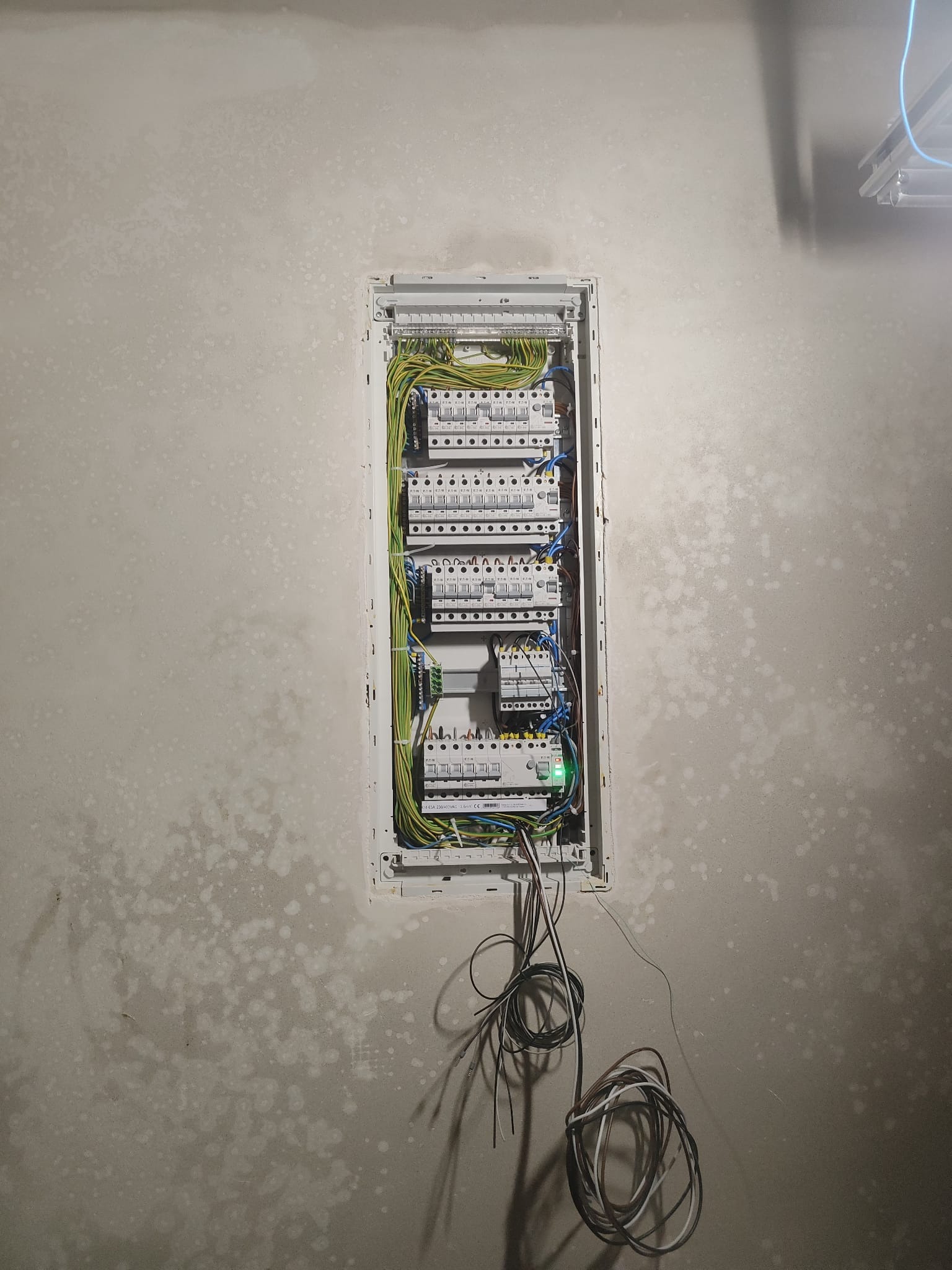 Wnętrze skrzynki rozdzielczej z zainstalowanymi bezpiecznikami i przewodami na tle surowej ściany w trakcie prac wykończeniowych.