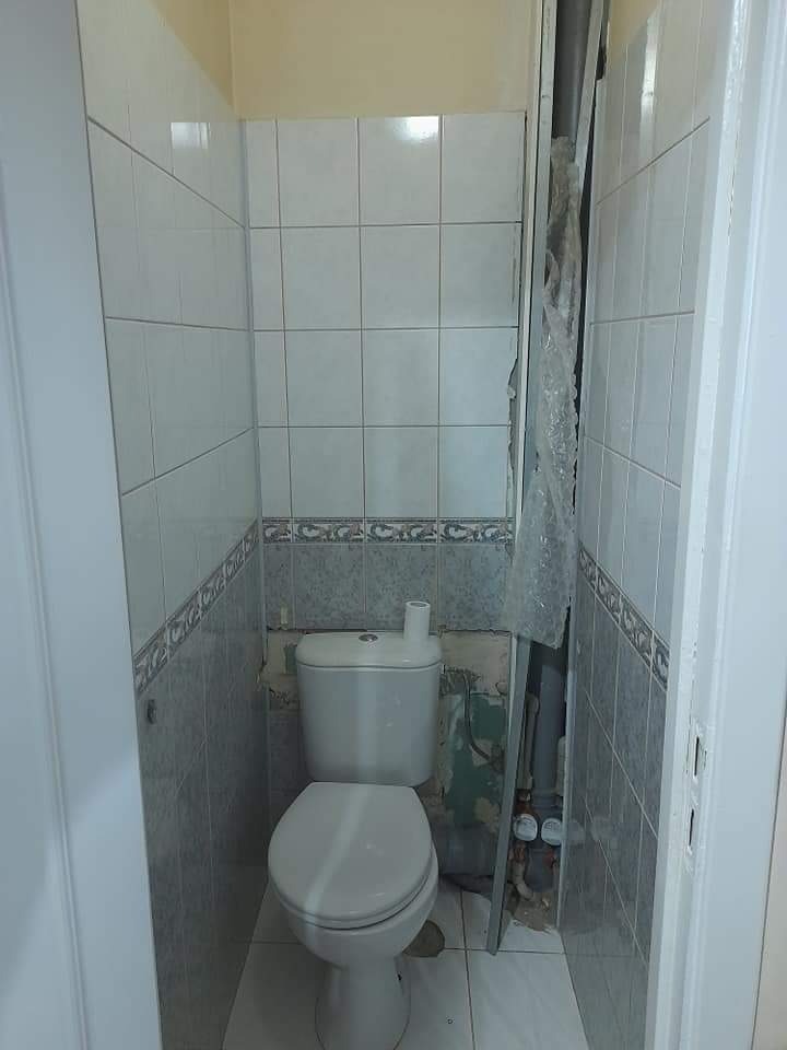 Toaleta w trakcie prac, widoczne odsłonięte fragmenty ścian, stare płytki częściowo usunięte, rury zabezpieczone folią.