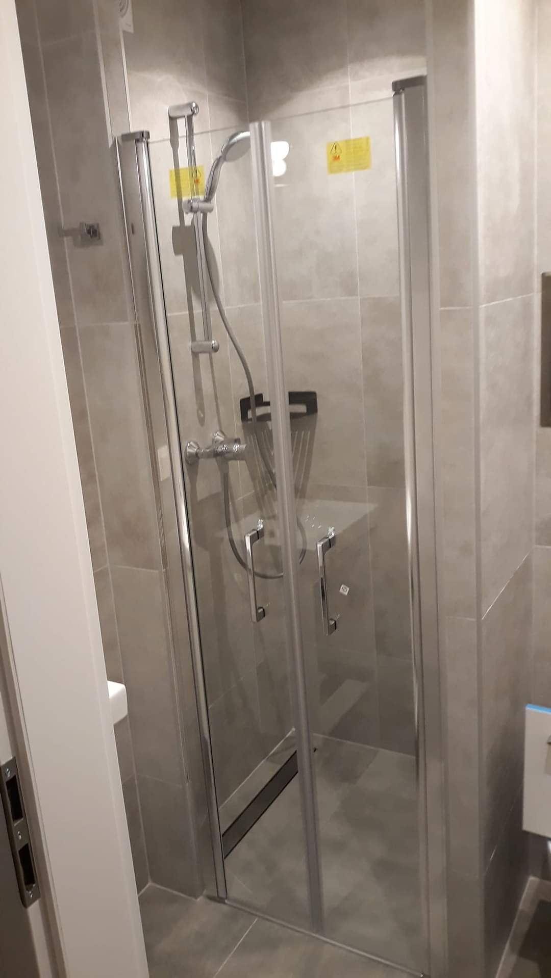 Nowoczesna kabina prysznicowa z szarymi płytkami, chromowaną armaturą i szklanymi drzwiami, widok z boku.