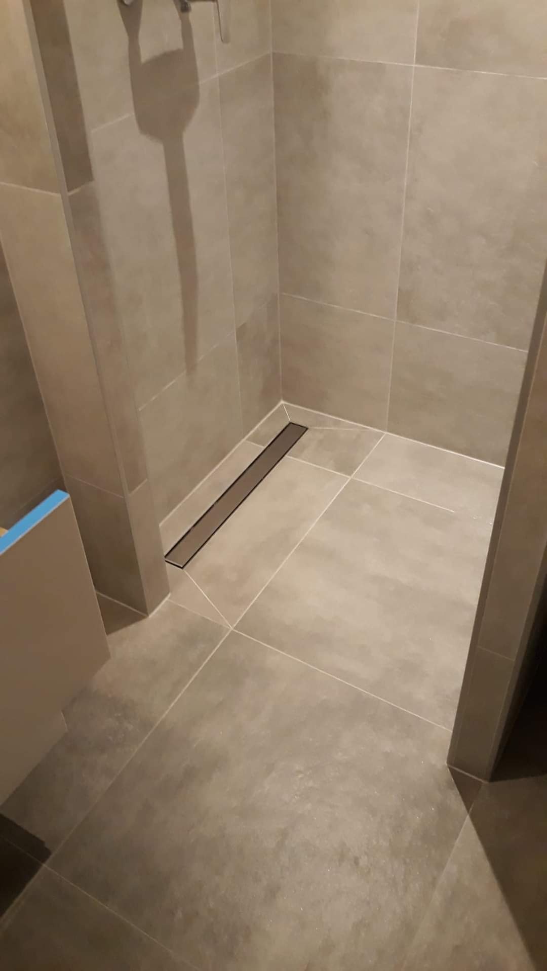 Nowoczesny odpływ liniowy w kabinie prysznicowej z jasnymi, kwadratowymi płytkami podłogowymi i ściennymi, minimalistyczny design.