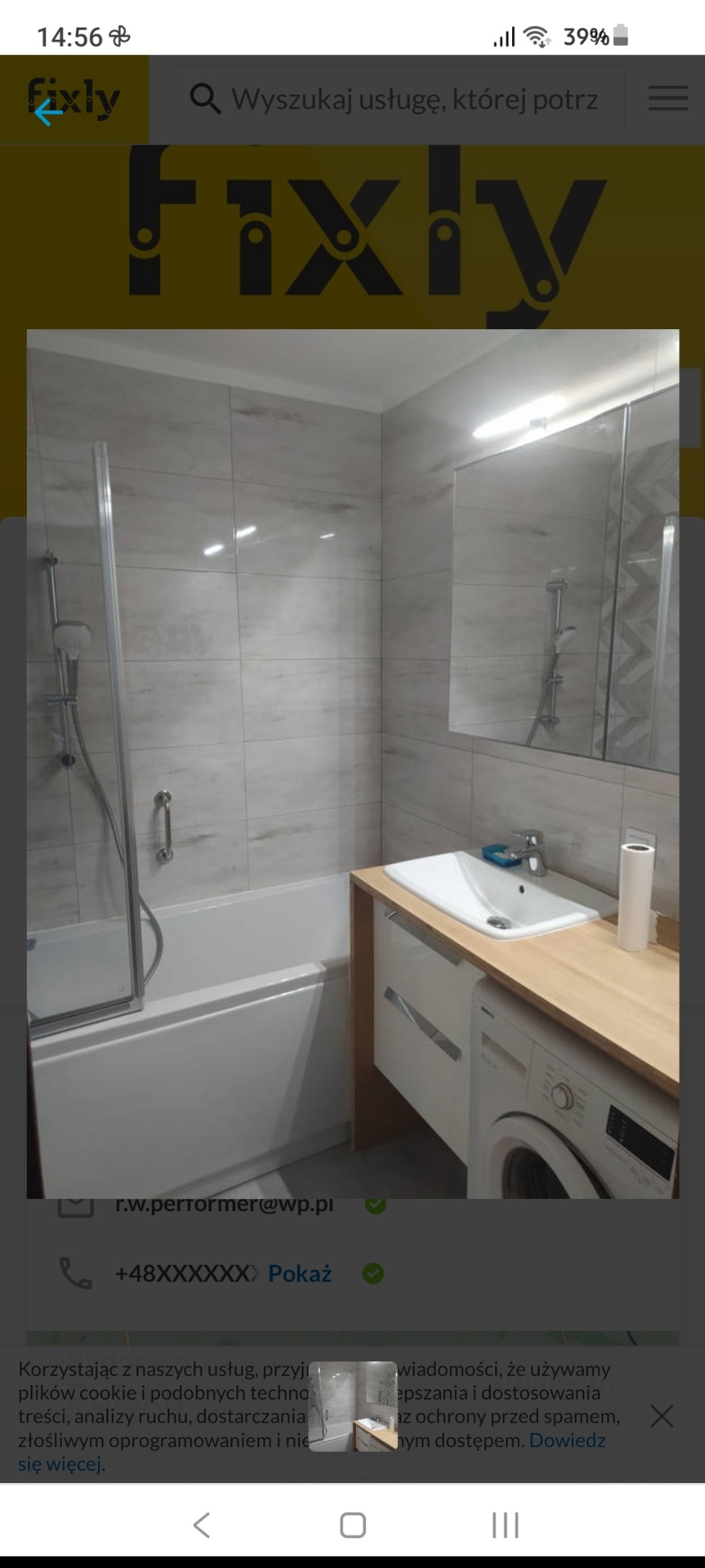 Nowoczesna łazienka z wanną z parawanem, umywalką nablatową na drewnianym blacie, pod którym znajduje się pralka. Ściany wyłożone płytkami imitującymi naturalny kamień.