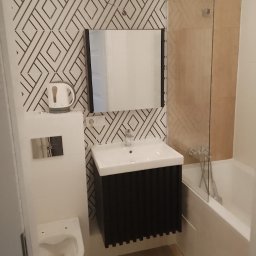 remontik - Nowoczesna łazienka z geometryczną tapetą, czarną szafką pod umywalką, wiszącą toaletą i parawanem nawannowym ze szkła hartowanego.