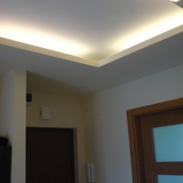 remontik - Nowoczesny sufit podwieszany z oświetleniem LED w narożniku, widok na fragment pokoju z drzwiami i domofonem na ścianie.