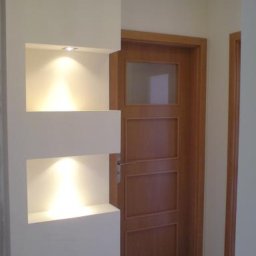 remontik - Nowoczesna wnęka ścienna z dwoma podświetlonymi półkami, obok drewniane drzwi wewnętrzne z szybą, kremowe ściany.