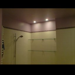 remontik - Wykończona łazienka z beżowymi płytkami, dekoracyjnym pasem mozaiki, szklanymi półkami i punktowym oświetleniem sufitowym w odcieniach fioletu.