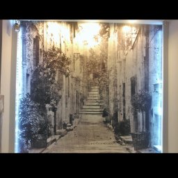 remontik - Fototapeta z podświetleniem LED prezentująca uliczkę w stylu śródziemnomorskim z roślinami w donicach.