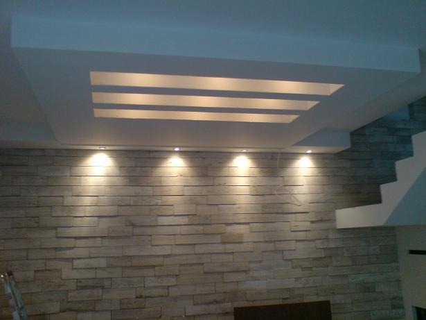 Nowoczesna ściana z kamienia dekoracyjnego podświetlona punktowymi lampami halogenowymi w suficie podwieszanym z oryginalnym oświetleniem liniowym.