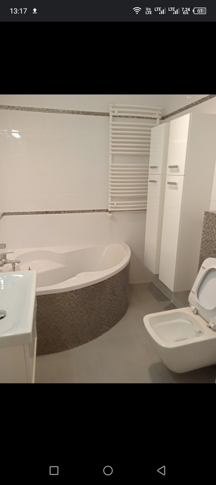 Nowoczesna łazienka po remoncie z wanną obudowaną mozaiką, białą armaturą, grzejnikiem drabinkowym i szafkami w zabudowie.