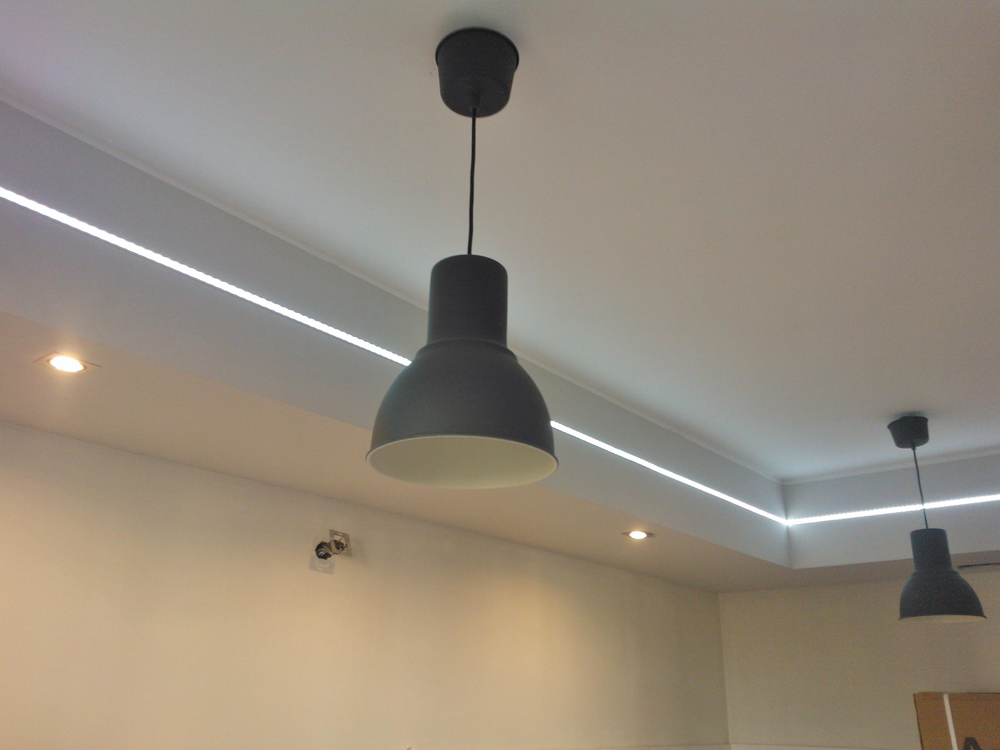 Nowoczesne oświetlenie sufitowe z dwoma wiszącymi lampami w stylu industrialnym i liniowym oświetleniem LED wzdłuż krawędzi sufitu.