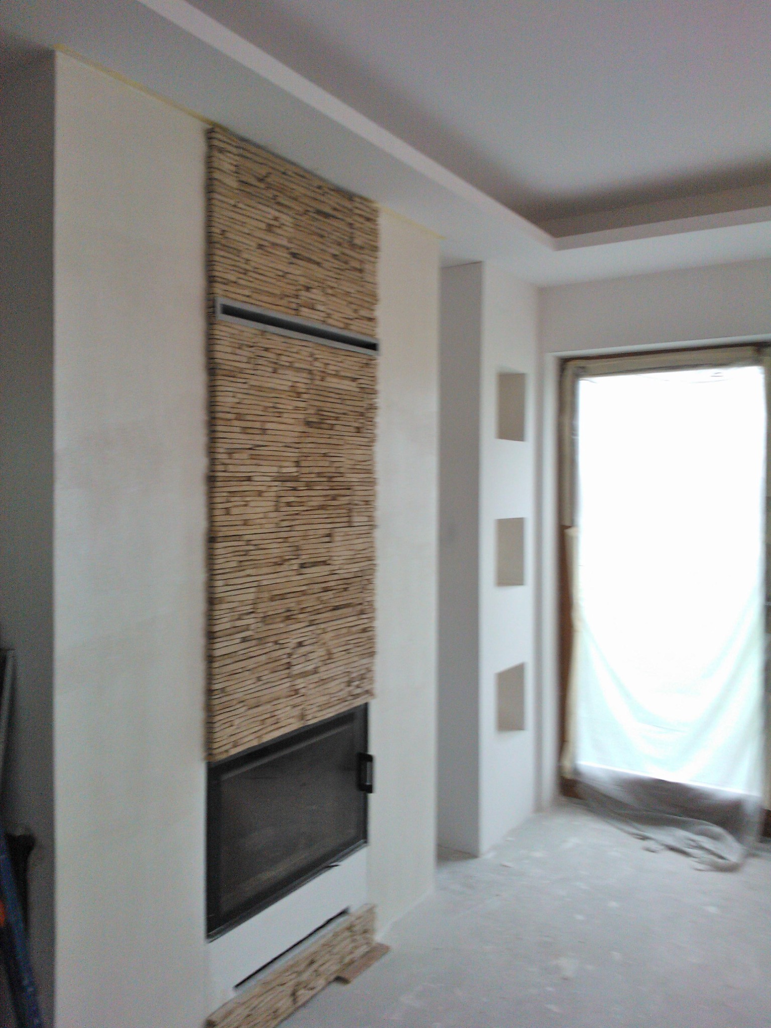 Ściana z dekoracyjną okładziną z drewnianych listewek nad kominkiem w surowym pomieszczeniu podczas wykańczania wnętrza.