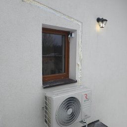 SWPM Szymon Witkowski Performance Management - Zewnętrzna jednostka klimatyzacji Rotenso zamontowana pod oknem na elewacji budynku z widocznymi śladami pianki montażowej wokół ramy okiennej.