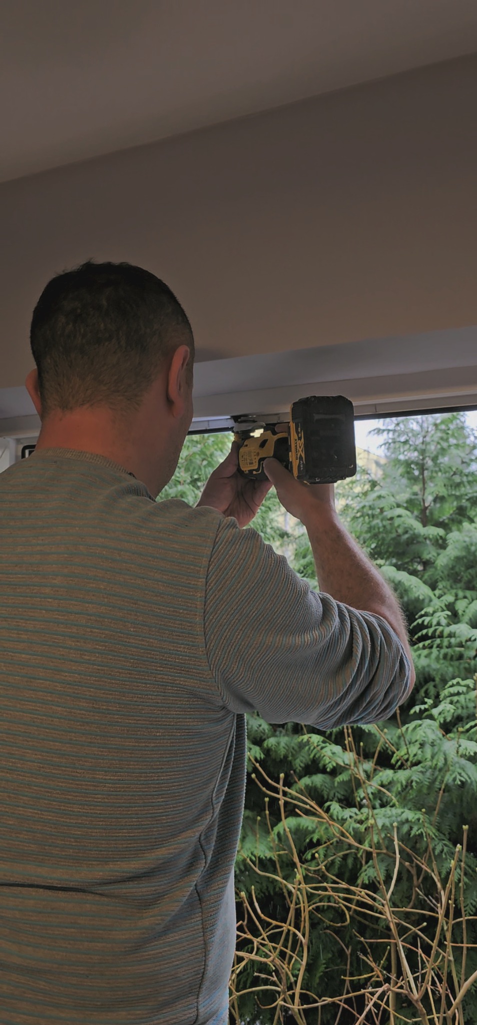 Elektryk mierzy napięcie w instalacji przy oknie za pomocą miernika zasilanego baterią DeWalt.