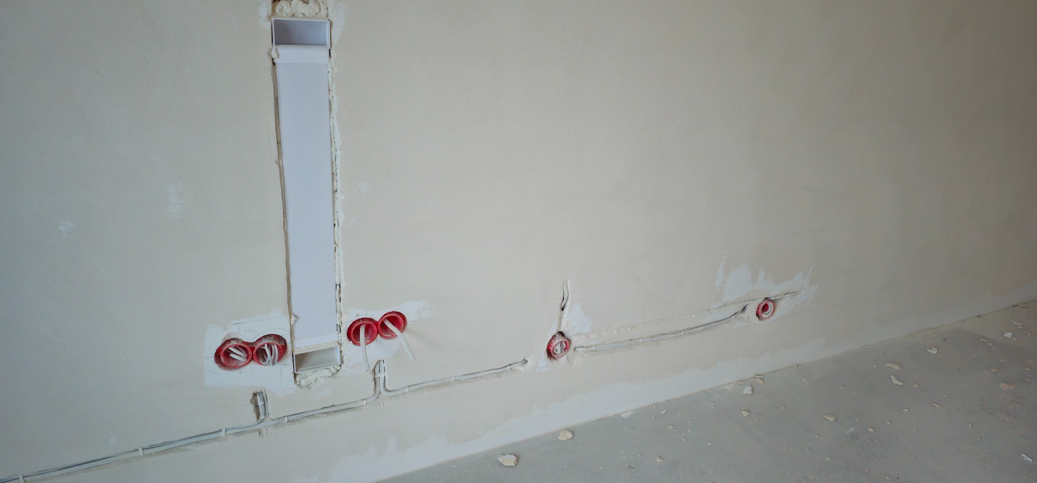 Przygotowanie do montażu gniazdek elektrycznych w ścianie, widoczne kable w peszlach i puszki instalacyjne w surowym stanie.