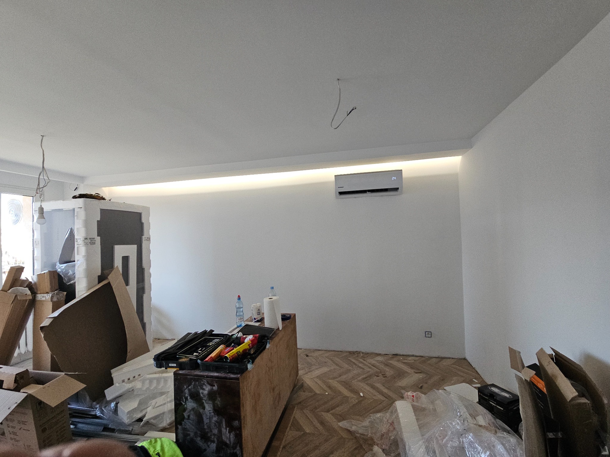 Wnętrze mieszkania w Łodzi w trakcie montażu klimatyzatora na ścianie, widoczne narzędzia i materiały budowlane, parkiet w jodełkę.