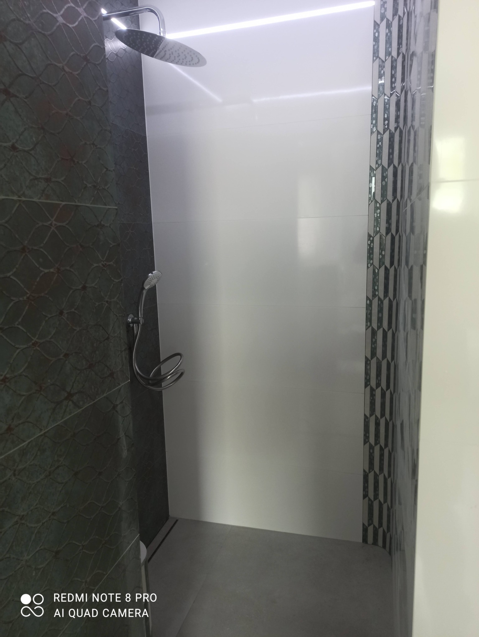 Nowoczesna kabina prysznicowa z deszczownicą, wykończona płytkami w odcieniach szarości i bieli, z dekoracyjnym wzorem na jednej ze ścian.