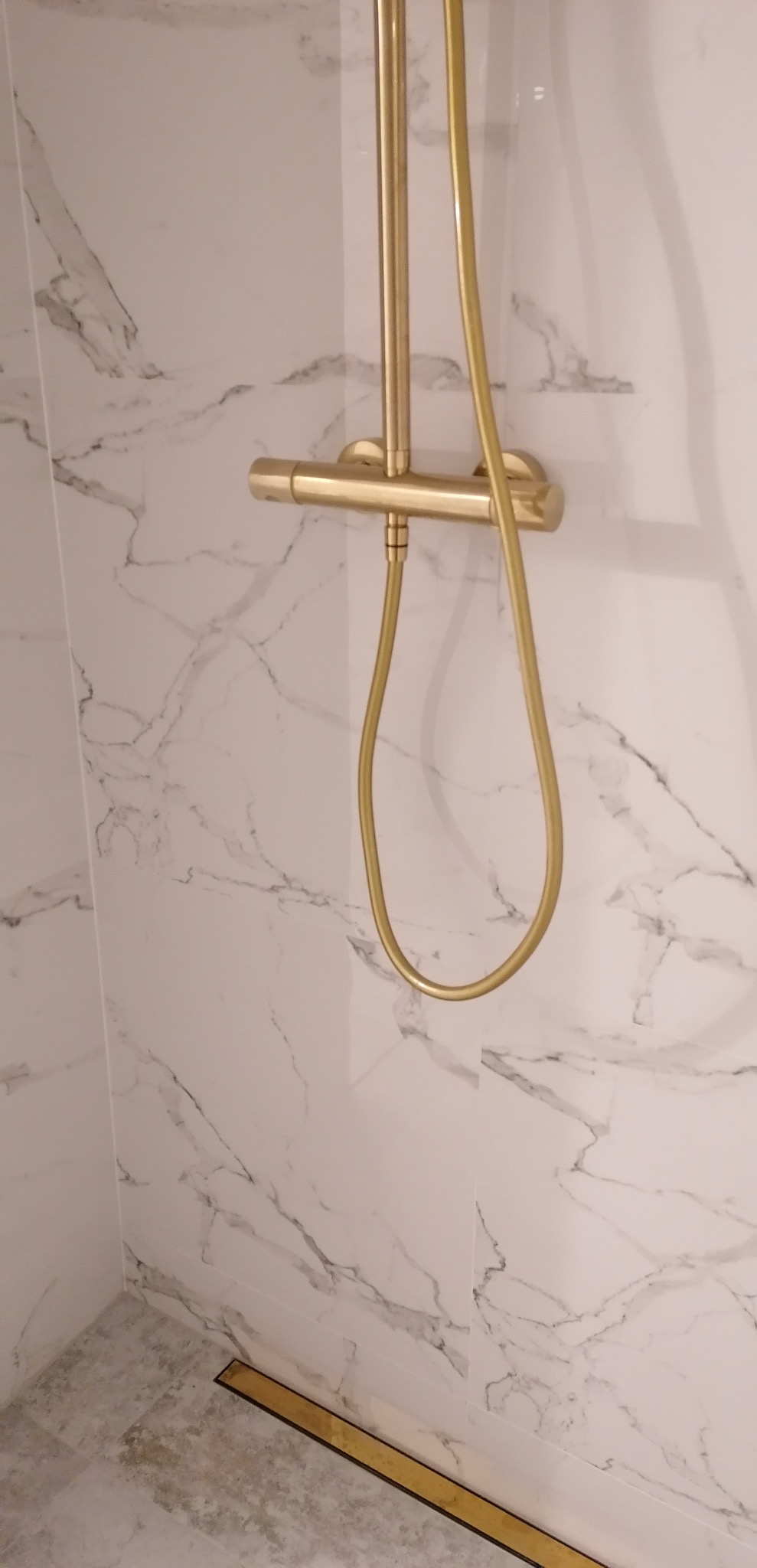 Wykończona łazienka z armaturą w kolorze złotym, marmurowe płytki ścienne, odpływ liniowy w podłodze.