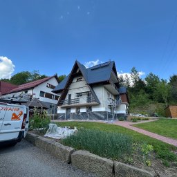 Minor Malowanie Dachów Natalia Szymczak - Dom w trakcie malowania elewacji, zabezpieczony folią, widoczny samochód firmy z logo i numerem telefonu. Prace elewacyjne w toku, rusztowania, częściowo pomalowany dach.