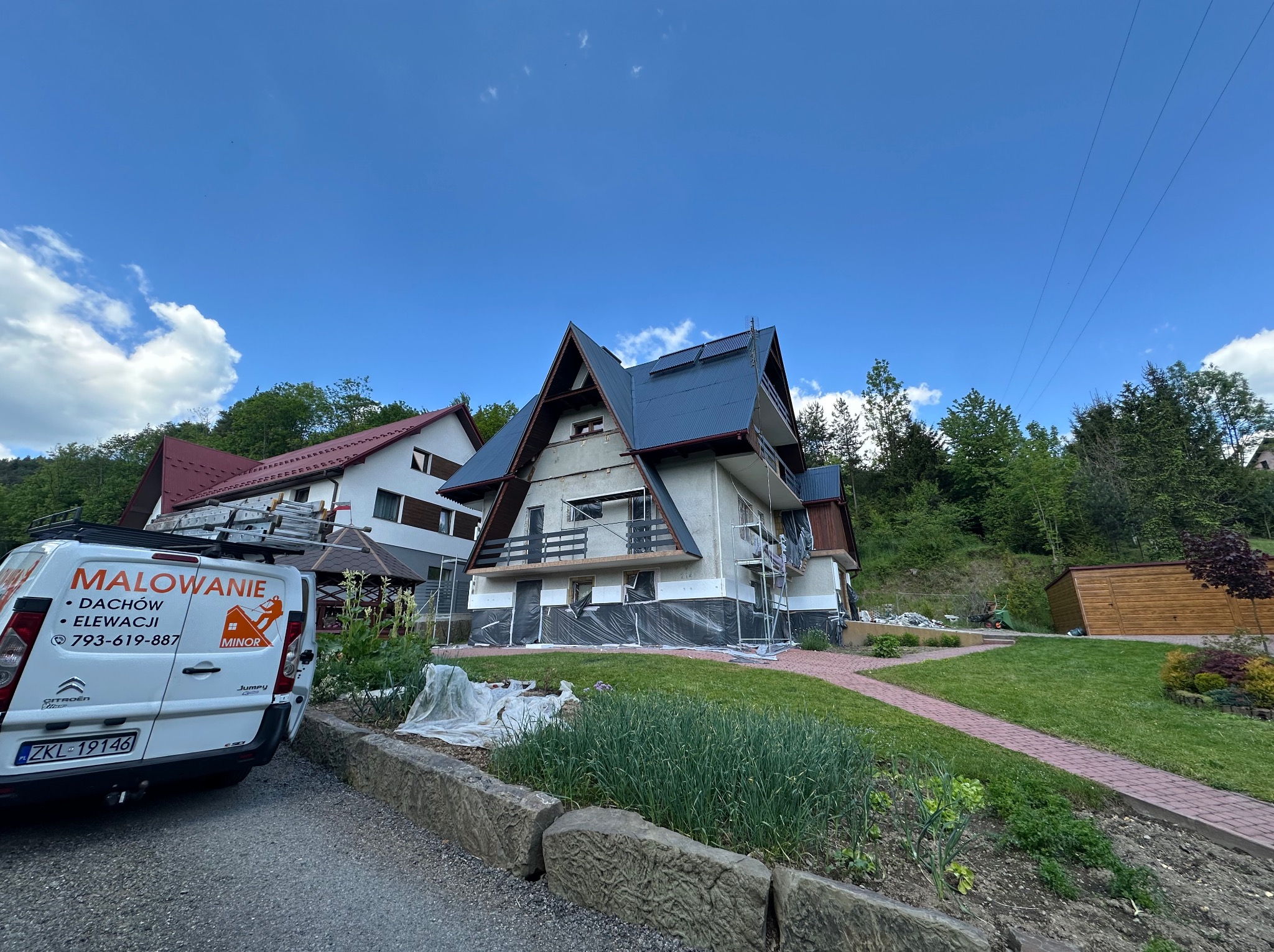 Dom w trakcie malowania elewacji, zabezpieczony folią, widoczny samochód firmy z logo i numerem telefonu. Prace elewacyjne w toku, rusztowania, częściowo pomalowany dach.