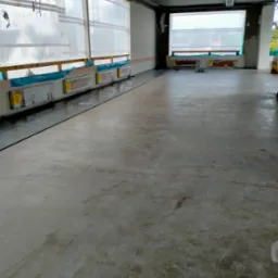 Betonowa wylewka podłoża w dużej hali, zabezpieczone okna folią, widoczne ślady po butach na powierzchni.