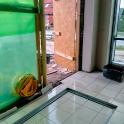 Wnętrze w Gorlicach w trakcie prac remontowych; widoczne zabezpieczenia folią, tymczasowe drzwi z płyty OSB, oraz przygotowany fragment pod wylewkę, z ramą z profili. Na podłodze białe płytki.