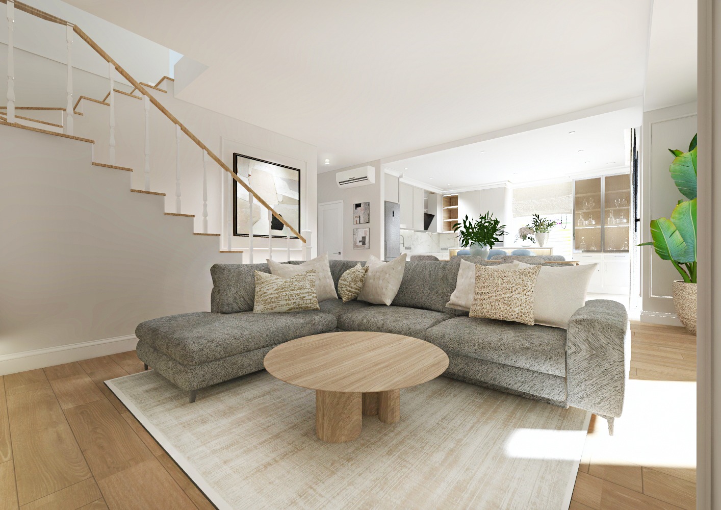 Jasne, przestronne wnętrze z szarym narożnikiem, okrągłym stolikiem kawowym i schodami. W tle widoczna kuchnia z białymi szafkami i marmurowym blatem. Na ścianie abstrakcyjny obraz w czarnej ramie.