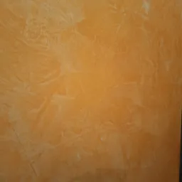 Teksturowana ściana w odcieniach pomarańczy i beżu, imitująca trawertyn, z widocznymi nierównościami i delikatnymi spękaniami.