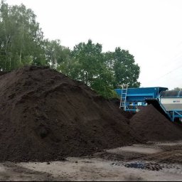 LATO-GARDEN - Góra ciemnej ziemi obok przesiewacza do gleby z drabiną, na tle drzew i linii energetycznych. Ślady opon na ziemi. Przesiewanie ziemi.