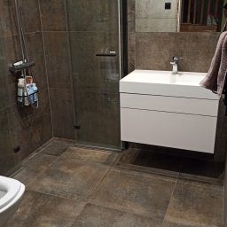 m4home Marcin Szmidt - Nowoczesna łazienka z kabiną prysznicową typu walk-in, brązowymi płytkami imitującymi kamień, białą szafką pod umywalką i lustrem z widocznym odbiciem schodów.