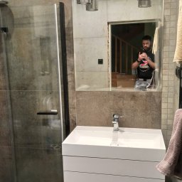 m4home Marcin Szmidt - Nowoczesna łazienka z kabiną prysznicową ze szkła, białą szafką pod umywalką i lustrem, w którym odbija się osoba robiąca zdjęcie.