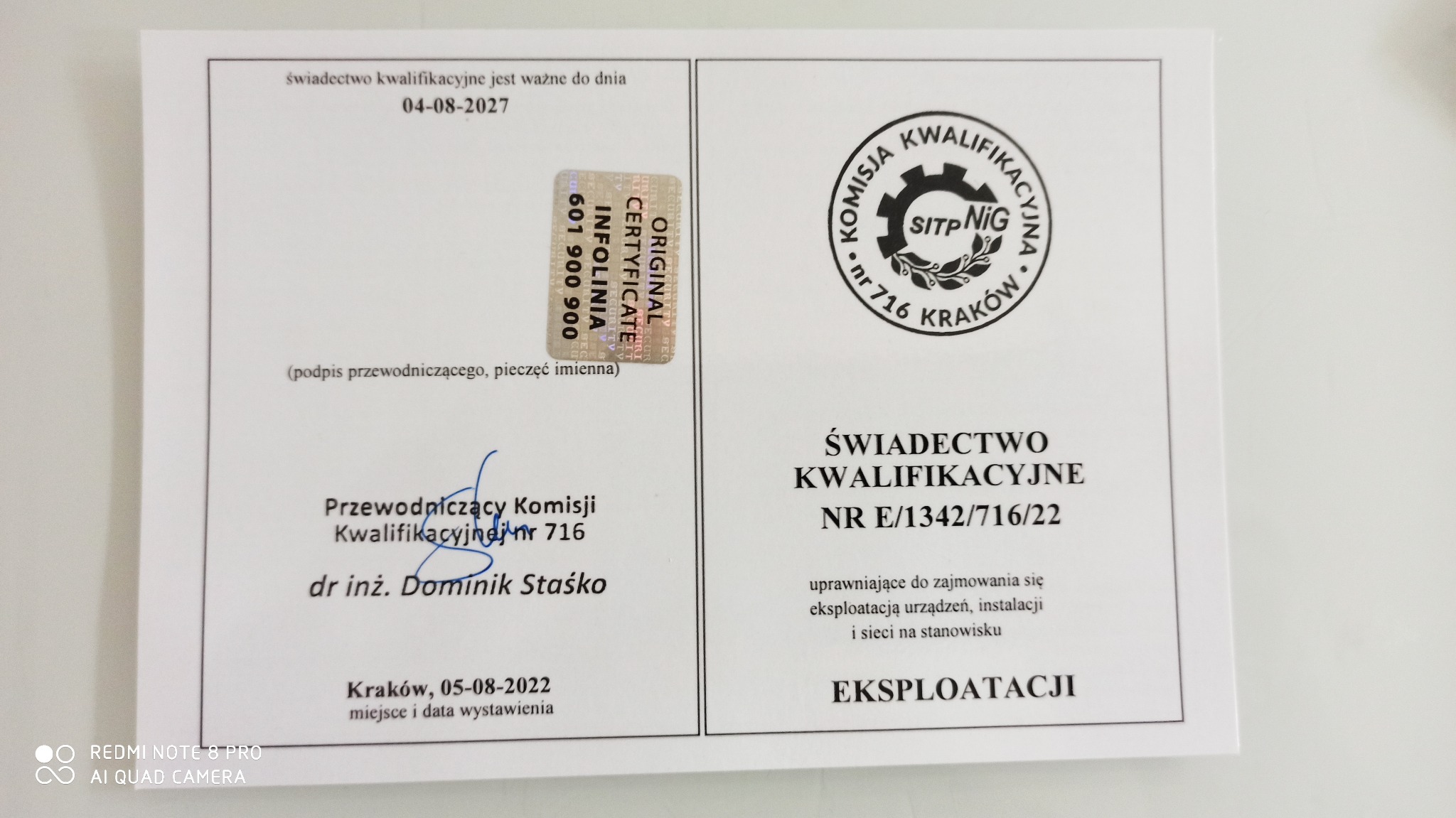 Skan świadectwa kwalifikacyjnego z hologramem, podpisem i datą ważności do 04-08-2027, uprawniającego do zajmowania się eksploatacją urządzeń, instalacji i sieci na stanowisku eksploatacji.