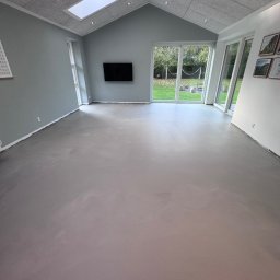 ProConcept - Jasnoszara wylewka samopoziomująca w przestronnym pokoju z oknami na ogród i sufitem z panelami akustycznymi oraz oknem dachowym. Minimalistyczny design.