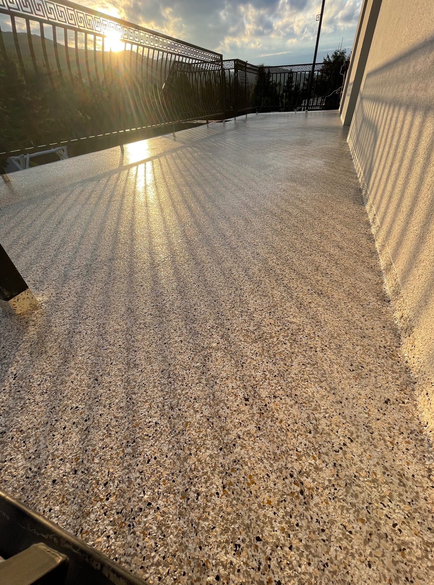 Błyszcząca, beżowa posadzka żywiczna na balkonie z metalową balustradą w promieniach zachodzącego słońca. Widok na góry w tle.