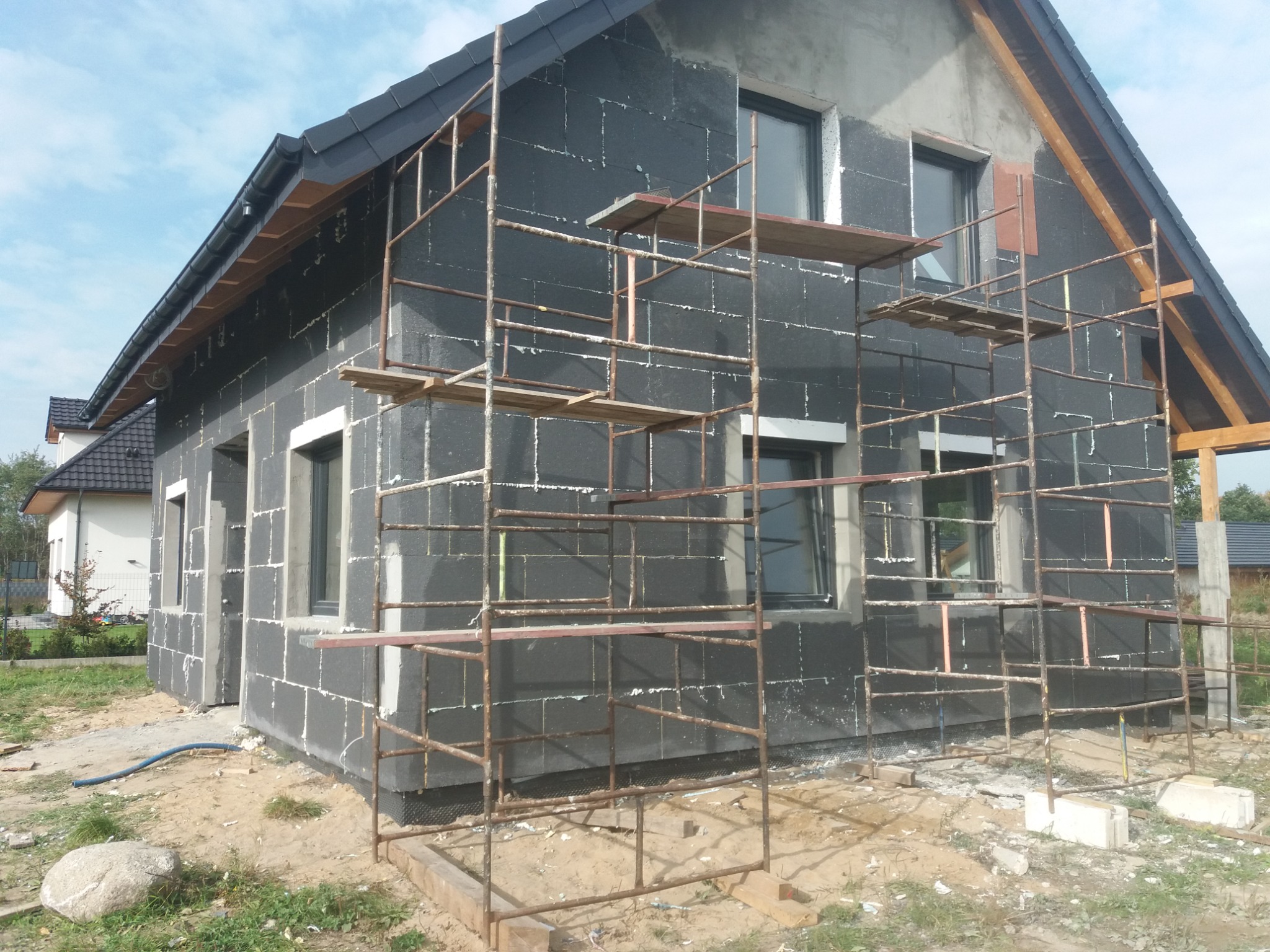 Dom w trakcie ocieplania styropianem grafitowym, widoczne rusztowanie i okna z szarymi ramami.