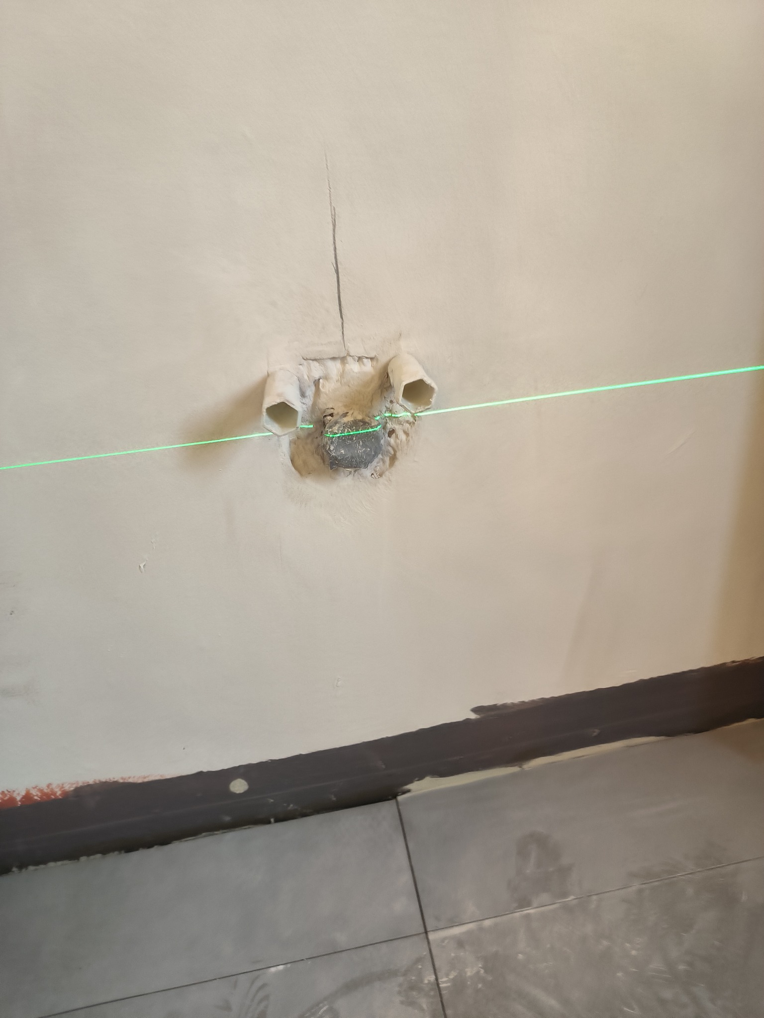 Przygotowanie ściany pod montaż instalacji sanitarnej, widoczne rury wystające ze ściany i zielona linia lasera wyznaczająca poziom.