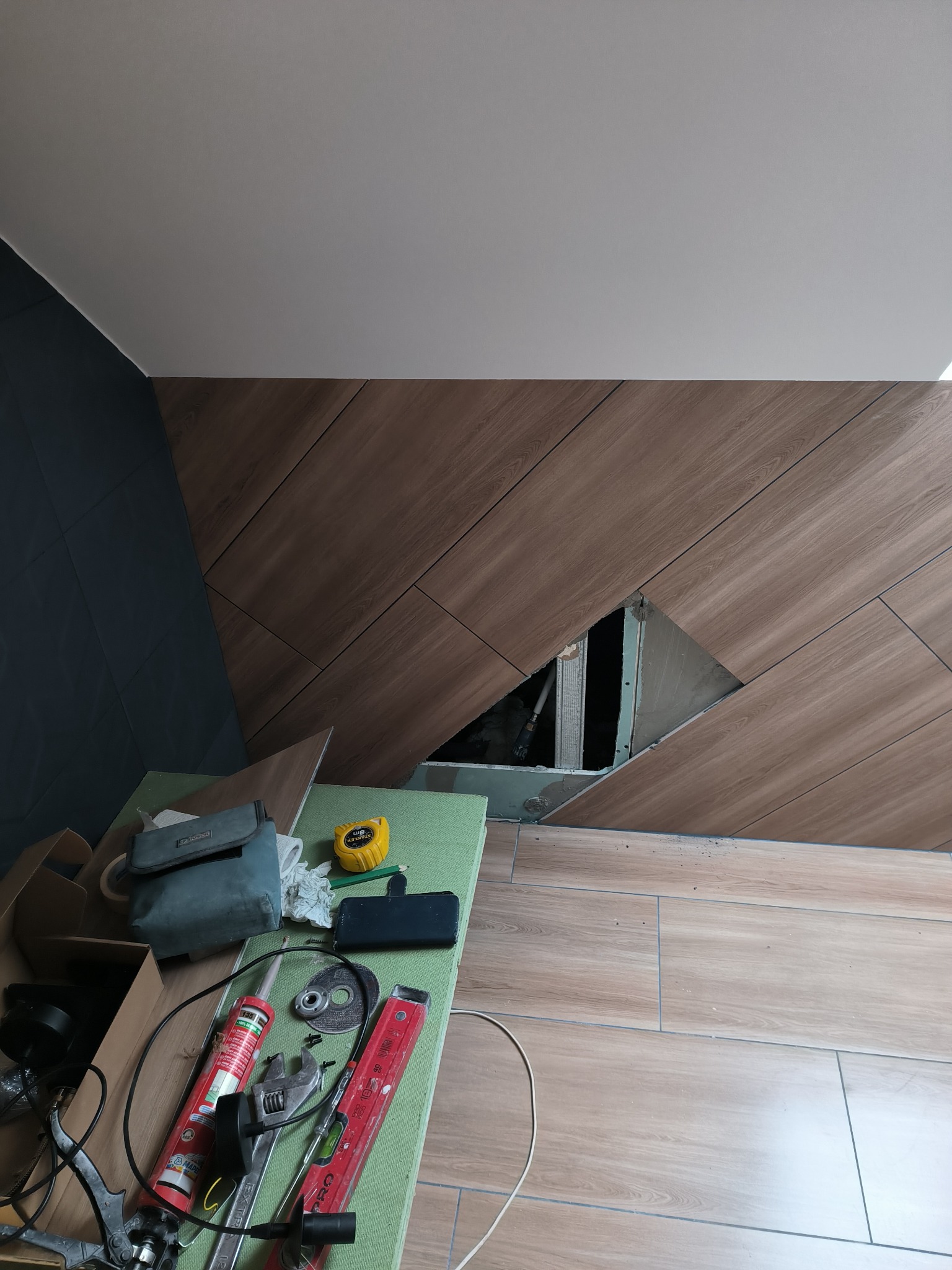 Układanie płytek imitujących drewno na ścianie w Cedyni, z widocznym otworem montażowym i narzędziami pracy na podłodze.