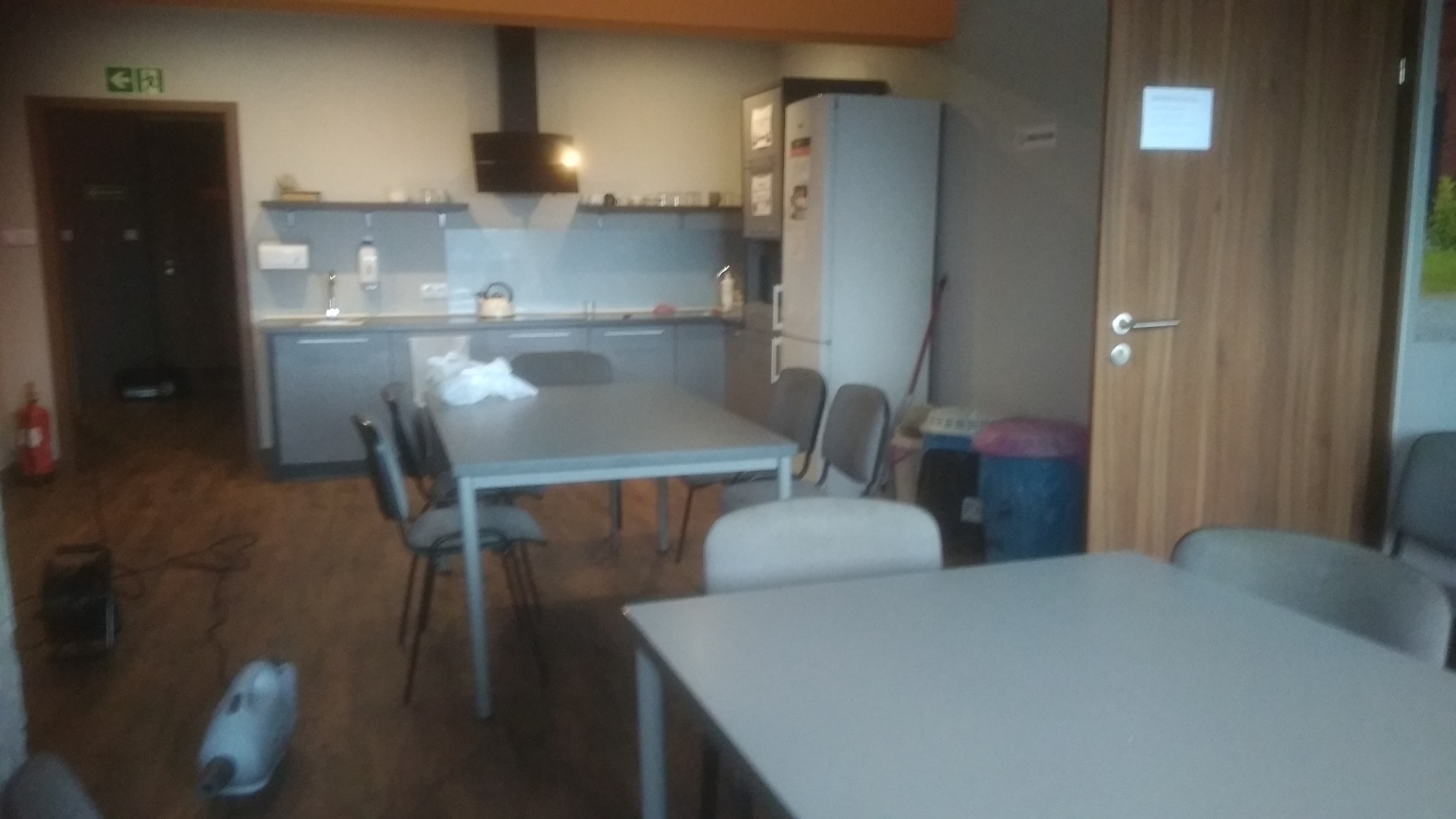 Wnętrze pomieszczenia socjalnego w Radomsku z wyposażoną kuchnią, stołami i krzesłami, widoczny sprzęt czyszczący sugerujący niedawne sprzątanie.