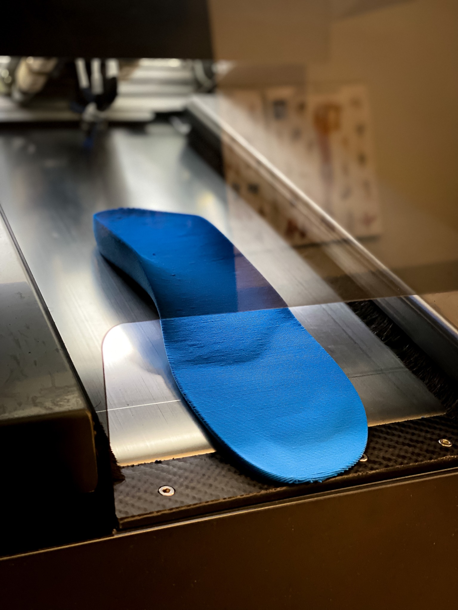 Niebieska, trójwymiarowa wkładka ortopedyczna z widoczną teksturą, umieszczona wewnątrz urządzenia, prawdopodobnie drukarki 3D, z widocznymi elementami konstrukcyjnymi i oświetleniem studyjnym.